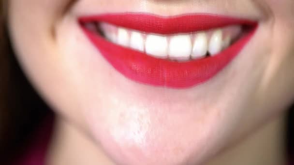 Sonrisa seductora y brillante de la chica de cerca, lápiz labial rojo en los labios, incluso dientes blancos como la nieve untados con lápiz labial rojo, una mujer sonríe, se muerde el labio juguetonamente — Vídeos de Stock