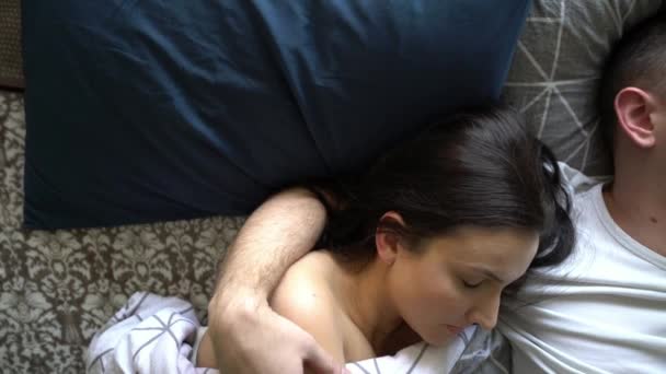 Ein junges Paar im Bett schläft gut. brünettes Mädchen umarmt ihren Mann in einem Traum, leichtes Bett, Familie schläft am Morgen, Mann hält seine Frau auf der Schulter, früher Morgen — Stockvideo