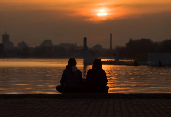 Rriends sitting together on the beach and watching sunset. Loving couple looking at the sun.