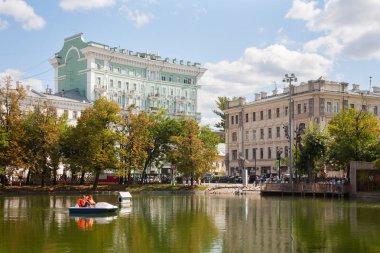 MOSCOW, RUSSIA - AUGUST 17, 2018: Pond, catamaran, trees and buildings in Chistoprudny Boulevard. This pond is called Chistye Prudy or Clean Ponds. clipart
