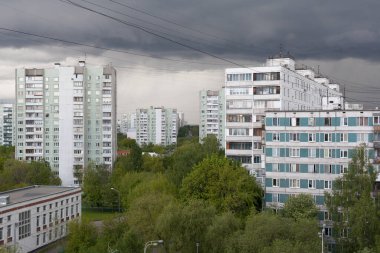 Moskova 'da bahar günü fırtınalı gökyüzüne karşı binalar ve yeşil ağaçlar