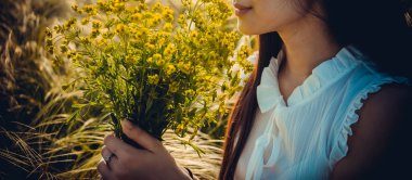 Yazın çimenlikte, gün batımında güneşli bir günde bir kız tarlada çiçek topluyor.