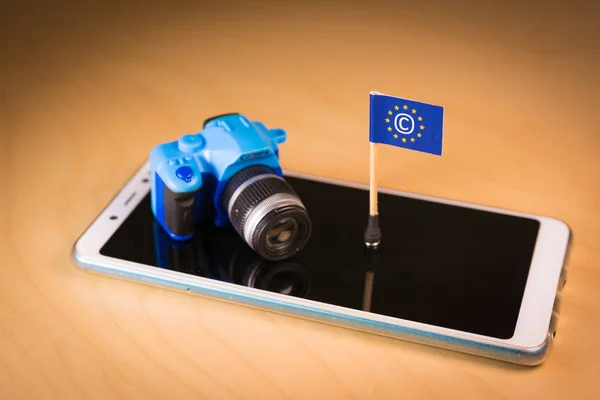 Flag with Copyright symbol and small camera over a smartphone. Symbolizing the EU Directive on Copyright in the Digital Single Market or CDSM. Art. 13 is known as meme ban