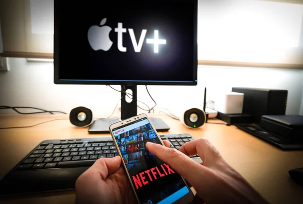 Barcelona, España. Marzo 2019: Hombre sostiene un teléfono inteligente con aplicación de netflix y un PC con el nuevo Apple TVplus en la pantalla — Foto de Stock