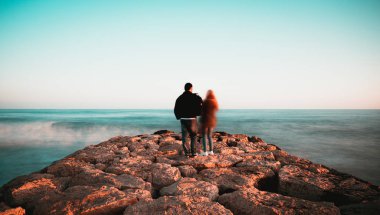 Sitges, Barcelona 'da taştan yapılmış bir iskelede duran genç çift. Yavaş fotoğraf çekimi.