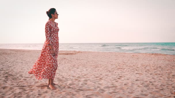 Slowmotion view of a beautiful woman in red dress smiling and looking to the mediterranean sea at sunset — Stock Video