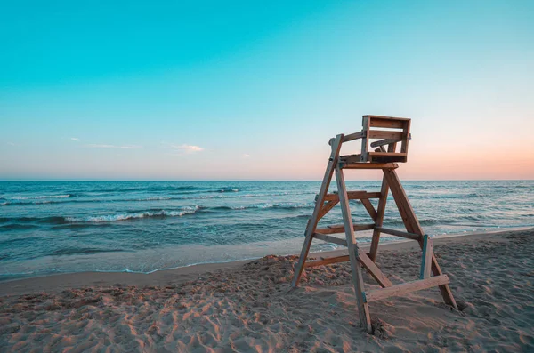 Praia com cadeira salva-vidas de madeira na hora do pôr do sol . — Fotografia de Stock