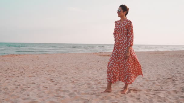 Slowmotion weergave van een mooie vrouw in rode jurk glimlachend en op zoek naar de Middellandse Zee bij zonsondergang — Stockvideo