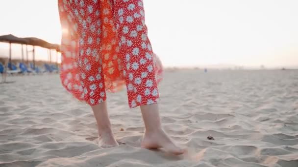 Primer plano de las piernas de la mujer en vestido rojo de pie en la playa al atardecer — Vídeos de Stock