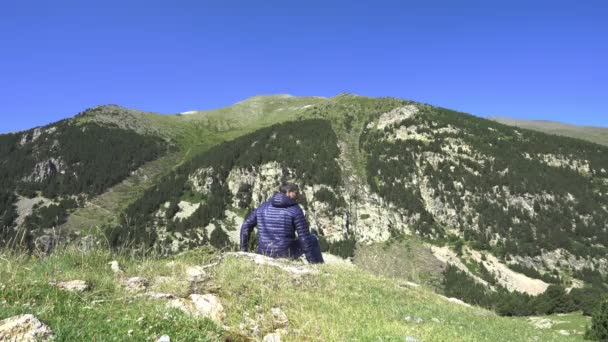 Muž v sportovním oblečení sedí na útesu a dívá se na Pyreneese. Podzim nebo letní krajina. — Stock video