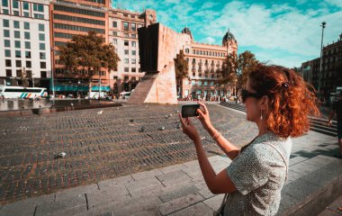 Plaza de Catalunya, Barselona'da akıllı telefonla fotoğraf çeken turist kadın.