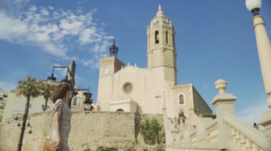 Covid-19 sırasında cerrahi maskeli güzel kıvırcık esmer turist fırında Sitges köyü ile birlikte.