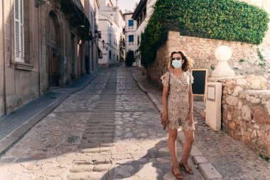 Barcelona 'nın Akdeniz köyü Sitges' de cerrahi maskeli güzel kıvırcık esmer turist.