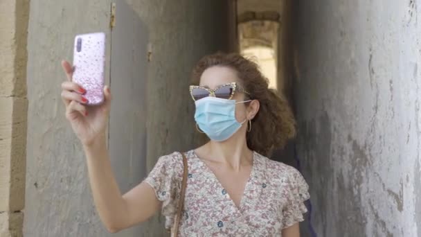 Gyönyörű göndör barna turista, sebészeti maszk vesz egy helyet a correlo de la rectoria Sitges, Spanyolország. — Stock videók