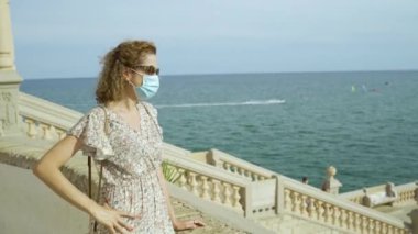 Covid-19 sırasında cerrahi maskeli güzel kıvırcık esmer turist fırında Sitges köyü ile birlikte.