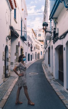 Barcelona 'nın Akdeniz köyü Sitges' de cerrahi maskeli güzel kıvırcık esmer turist.