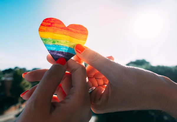 Lesbiana pareja cogida de la mano y un arco iris corazón — Foto de Stock