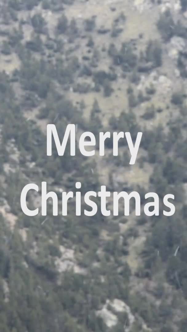 Vídeo vertical de texto de Feliz Navidad con copos de nieve cayendo y las montañas en el fondo — Vídeos de Stock