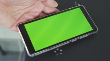 Masada yeşil ekranlı akıllı telefon tutan bir adam.