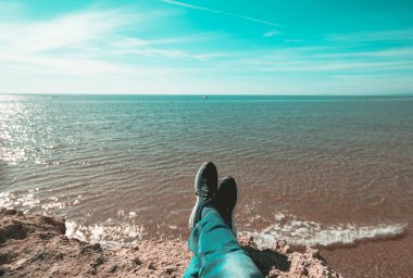 Mavi denizin üzerinde bir uçurumun kenarında oturan bir yürüyüşçüden çekilen ilk kişi.