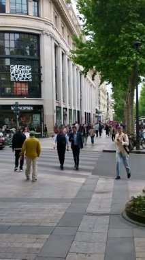 Paris, France. May 14, 2025, People walking on the sidewalk in front of Galeries Lafayette Champs Elysees in Paris