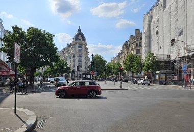 Paris, France. May 14, 2025, Red car driving through intersection in Paris, France, with typical Haussmann architecture and street scene