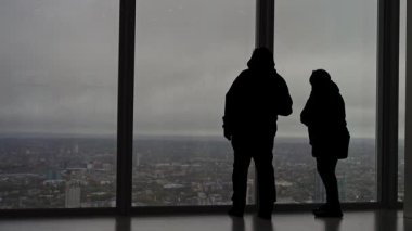 Silhouetted and anonymous tourists enjoying panoramic view of London from high rise observatory