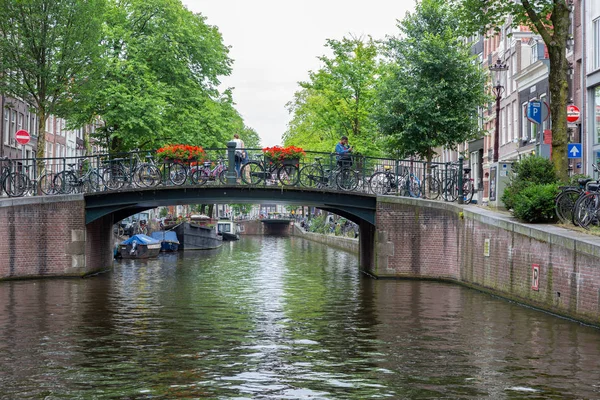 Амстердамский канал с видом на мост с велосипедами и людьми — стоковое фото