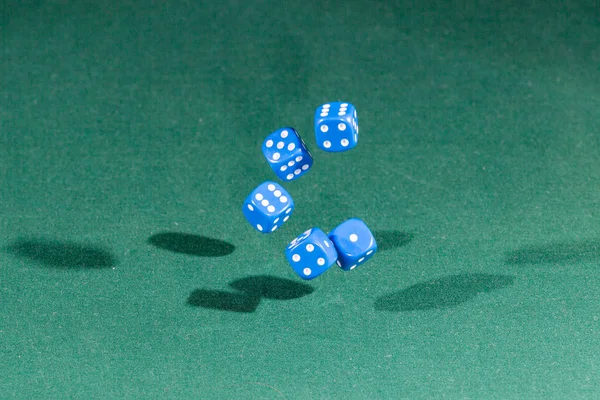 Пять синих кубиков, падающих на зеленый стол — стоковое фото