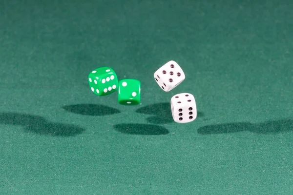 Four white and green dices falling on a green table