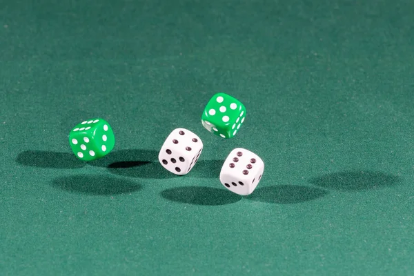 Four white and green dices falling on a green table
