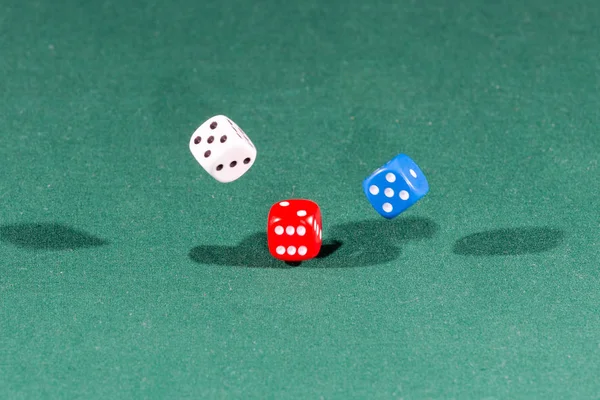 Белые, красные и синие кубики падают на зеленый стол — стоковое фото