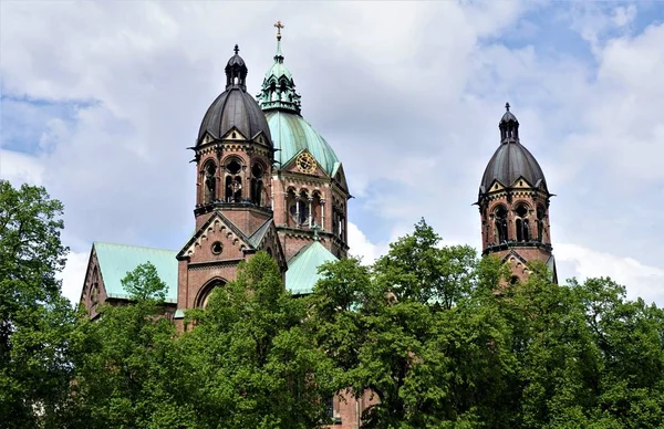 As torres e a cúpula da igreja de São Lucas em Munique atrás das árvores — Fotografia de Stock
