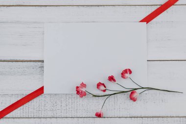 Boş beyaz kartı süslemeleri ile kırmızı kağıt çiçekler ve kırmızı kurdele Beyaz ahşap zemin üzerinde