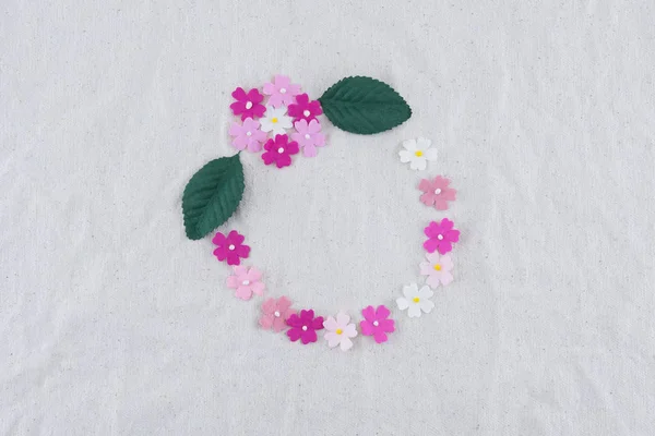 Round wreath made from pink tone paper flowers and green leaves on muslin fabric with copy space