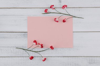 Boş pembe kart süslemeleri Beyaz ahşap zemin üzerinde kırmızı kağıt çiçeklerle 