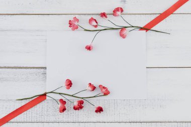 Boş beyaz kartı süslemeleri ile kırmızı kağıt çiçekler ve kırmızı kurdele Beyaz ahşap zemin üzerinde