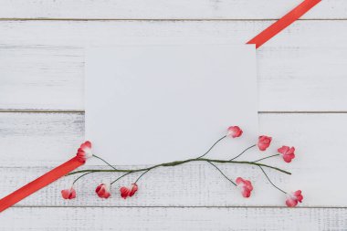 Boş beyaz kartı süslemeleri ile kırmızı kağıt çiçekler ve kırmızı kurdele Beyaz ahşap zemin üzerinde
