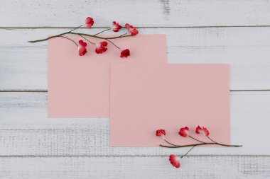 İki boş pembe kart süslemeleri Beyaz ahşap zemin üzerinde kırmızı kağıt çiçeklerle 
