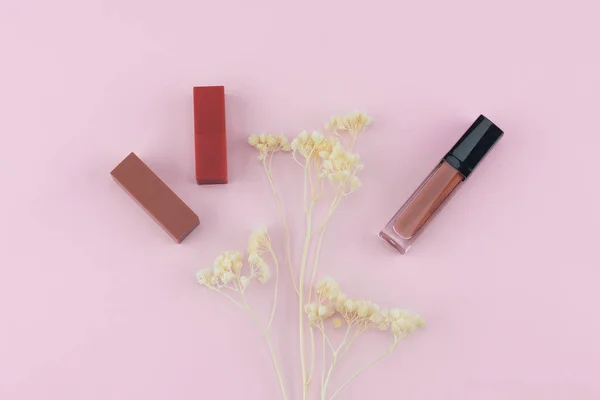 Ruj ve dudak parlatıcısı pastel pembe bir arka plan üzerinde beyaz Kuru çiçekler ile süsleyin