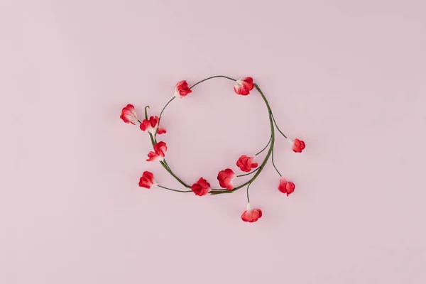 Round wreath made from red paper flowers with branch on pink background with copy space