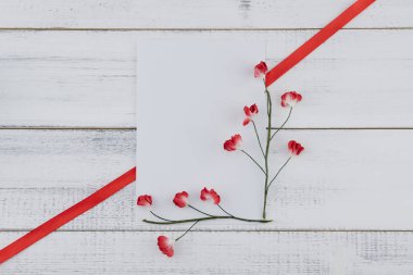 Boş beyaz kartı süslemeleri ile kırmızı kağıt çiçekler ve kırmızı kurdele Beyaz ahşap zemin üzerinde