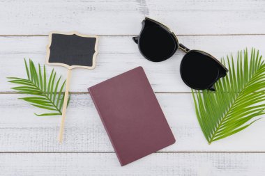 Güneş gözlüğü, küçük Pano ve pasaport eğreltiotu yaprakları üzerinde beyaz tahta arka plan ile