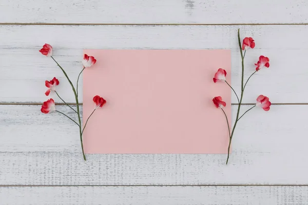 ピンクのダミーカードを飾る白いウッドの背景に赤の紙の花 — ストック写真