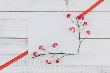 Boş beyaz kartı süslemeleri ile kırmızı kağıt çiçekler ve kırmızı kurdele Beyaz ahşap zemin üzerinde