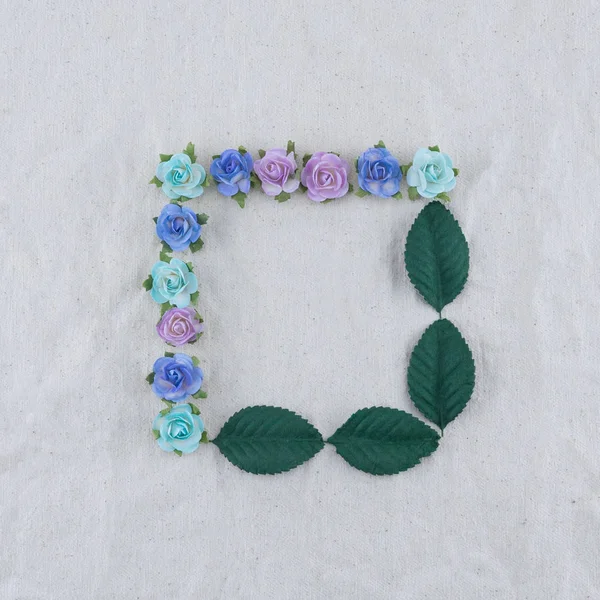 Square wreath made from blue tone rose paper flowers and green leaves on muslin fabric with copy space