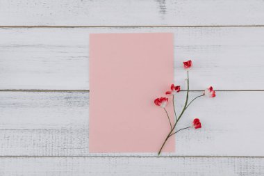 Boş pembe kart süslemeleri Beyaz ahşap zemin üzerinde kırmızı kağıt çiçeklerle 