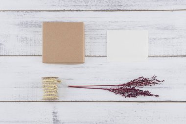 Kahverengi hediye kutusu, beyaz küçücük oyun kağıdı, kahverengi ip ve menekşe kurutulmuş çiçek buketi Beyaz ahşap zemin üzerinde