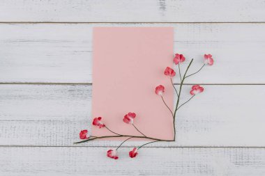Boş pembe kart süslemeleri Beyaz ahşap zemin üzerinde kırmızı kağıt çiçeklerle 