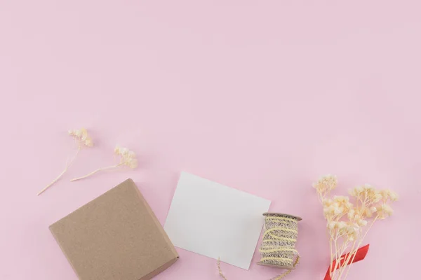 Boş beyaz kartı, kahverengi hediye kutusu ve ip kopya alanı pastel pembe zemin üzerine beyaz Kuru çiçekler Buket ile süsleyin